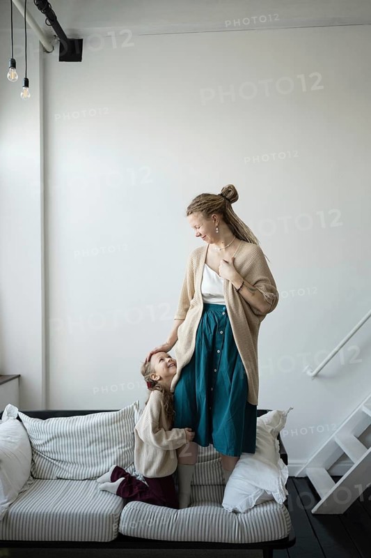 A mother and daughter share a joyful moment on a cozy couch The mother fondly looks down at her daughter, who is smiling back with love The scene exudes warmth and affection