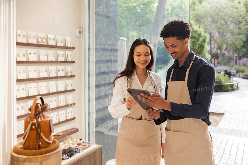 Retail employees in a stylish bag store use a tablet to enhance customer service. The bright interior, filled with various accessories, creates an inviting shopping atmosphere