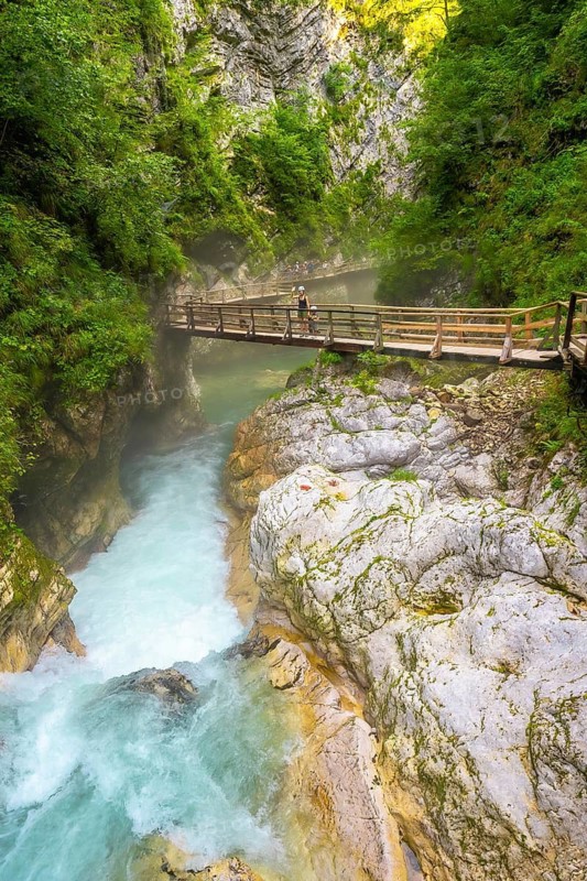 Tourists enjoying a scenic walk along a wooden footbridge over the vibrant radovna river in vintgar gorge, slovenia
