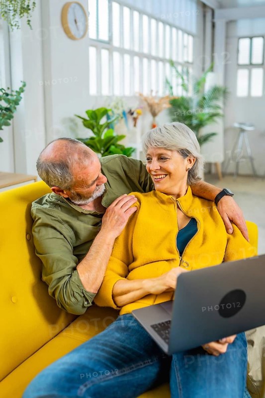 Happy senior couple planning and booking holidays using laptop at home