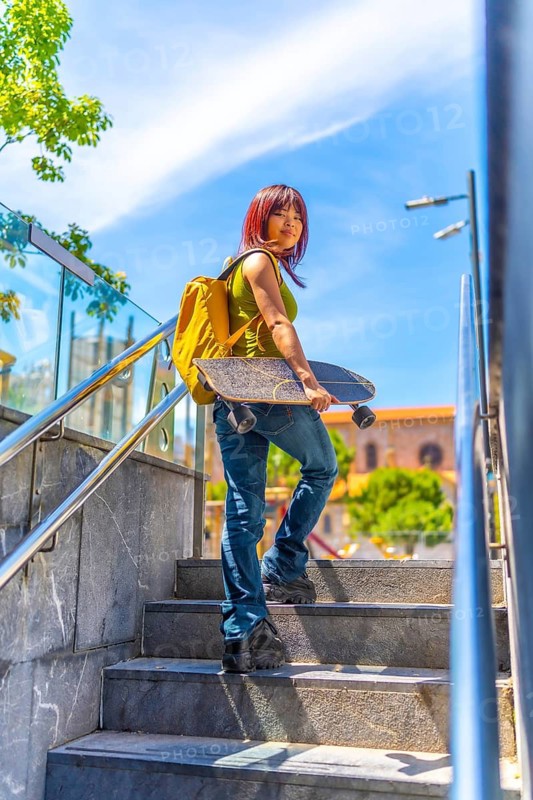 Vertical photo of the rear view of a chinese cool young woman carrying skateboard turning while walking up stairs in the city