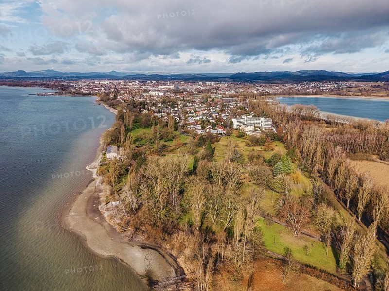 Aerial view of the Mettnau peninsula in western Lake Constance with winter vegetation with the Mettnaupark, Mettnaukur, behind it the town of Radolfzell, the Hegauberge Mountains on the horizon, Konstanz district, Baden-Württemberg, Germany