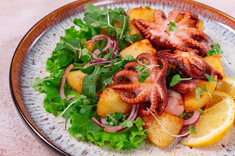 Grilled octopus with baked potatoes and fresh herbs, on a decorative plate, homemade
