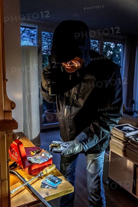 Symbolic image of a burglary, perpetrator has broken into a flat from the garden side and is looking for loot, breaks open a cash box, finds valuables, money
