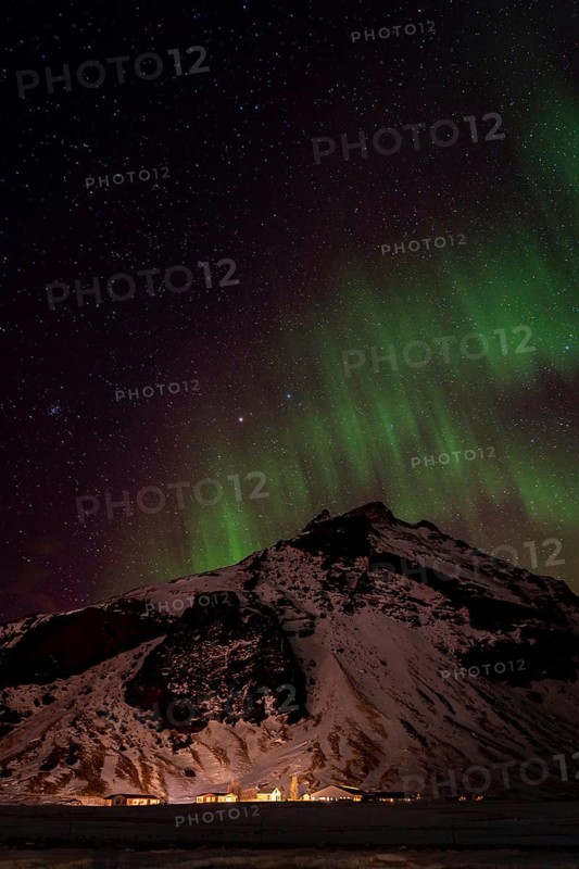 Experience the awe of the Northern Lights casting a green glow over a snow-covered mountain in Iceland. A serene nighttime landscape showcasing nature's beauty