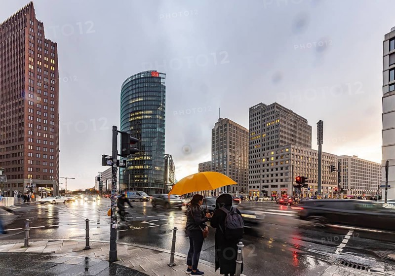 Potsdamer Platz Berlin in the evening with traffic on the streets. When it rains, the skyscrapers are reflected in puddles of water. People traveling with umbrellas. Berlin, Germany