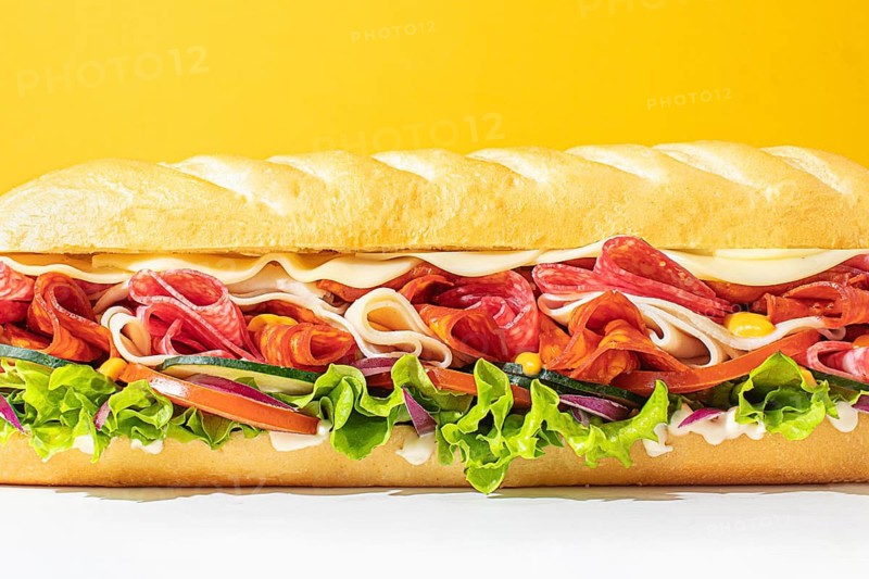 Close-up of a stacked deli sandwich, styled on a vibrant monochrome backdrop, with frontal lighting to emphasize depth and detail