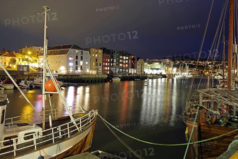 Boats in illuminated nocturnal harbor next to colorful buildings and calm water, Nidelva, Trondheim, Tröndelang, Norway