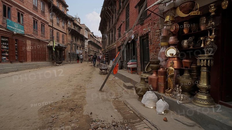 A busy old town street with shops, with a supported façade selling copperware and people walking, Kathmandu after the earthquake, Nepal