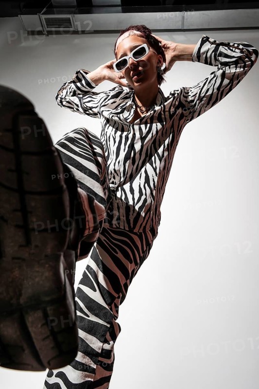 Model poses confidently in animal print attire, captured with dramatic flash photography in a studio setting. The low angle adds a dynamic and edgy feel
