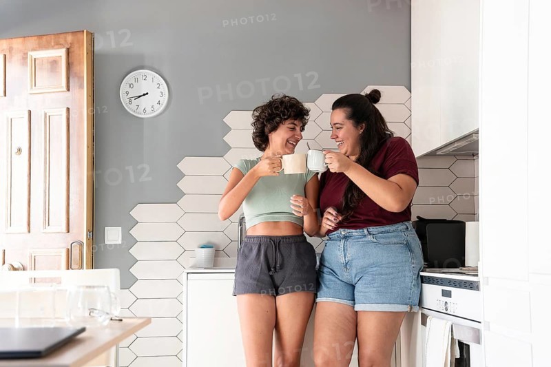 A cheerful lesbian couple shares a coffee break in their stylish kitchen. They enjoy a moment of laughter and connection, creating a relaxed, happy atmosphere