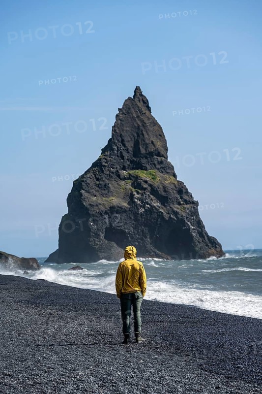 Tourist on black beach, rock Reynisdrangar in water, at Reynisfjara beach, Vik, South Iceland, Iceland
