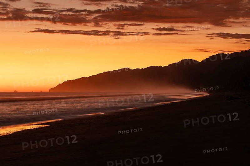 After sunset, the deep red sky glows above palms and ocean spray with views of Corcovado National Park. Costa Rica