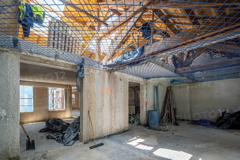 Interior view of a building under construction. Tools, safety netting, and equipment are visible, highlighting the ongoing renovation process and construction environment