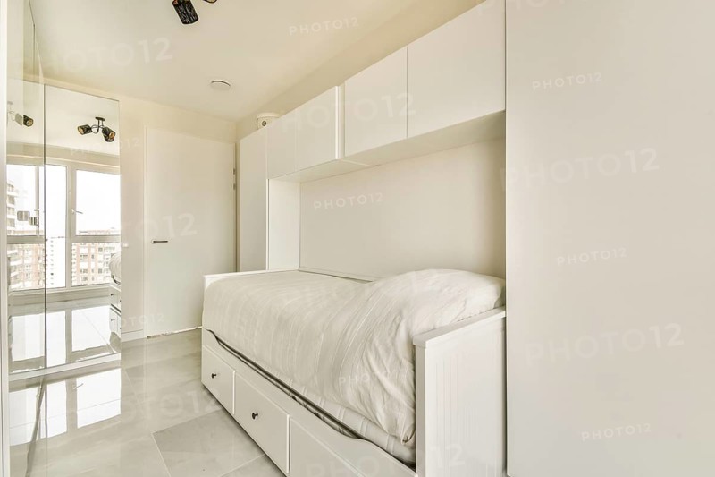 Modern minimalist bedroom with a loft bed and built-in storage, featuring clean lines, white furniture, and ample natural light from large windows for a tranquil atmosphere