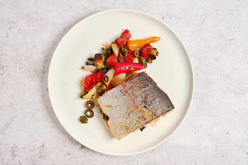 Piece of oven roasted sea trout with vegetables on a plate, top view