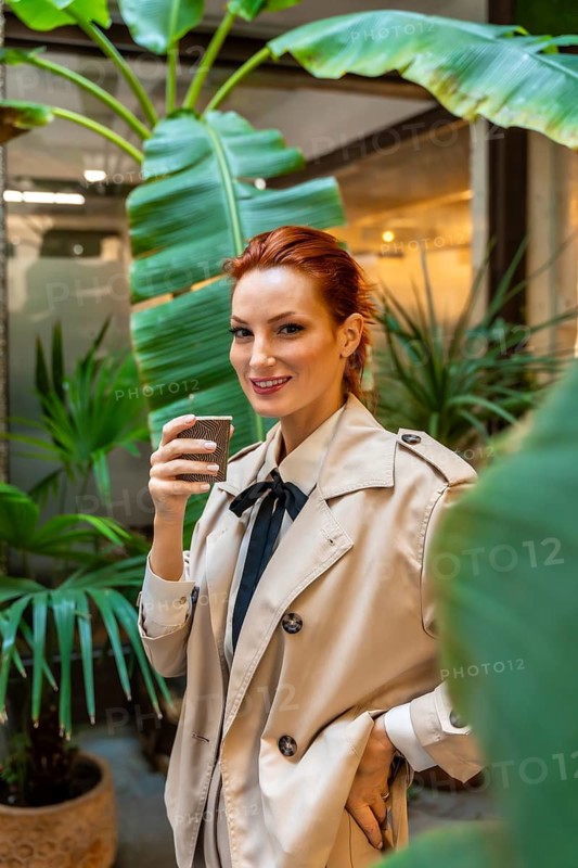 Vertical portrait of a chic woman standing drinking coffee at the entrance of the office