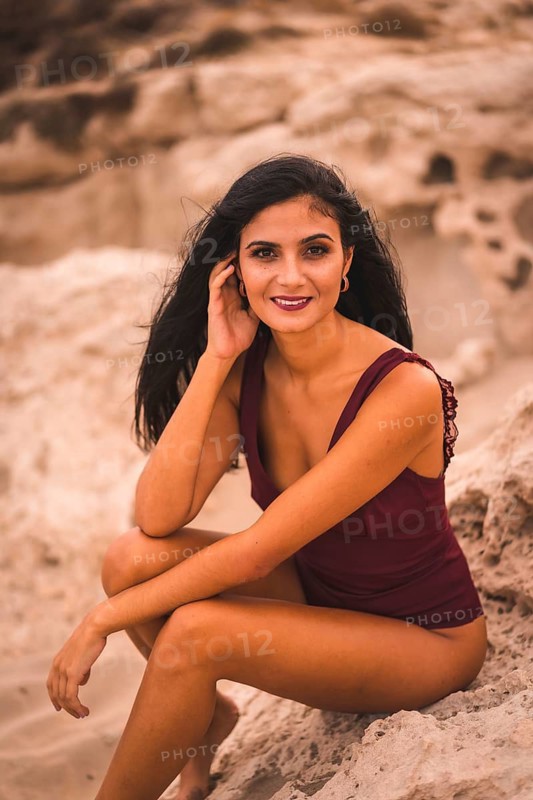 Portrait of a young brunette Caucasian woman in a maroon swimsuit, sitting smiling on the beach of Cabo de Gata, Nijar. Andalucia, Spain
