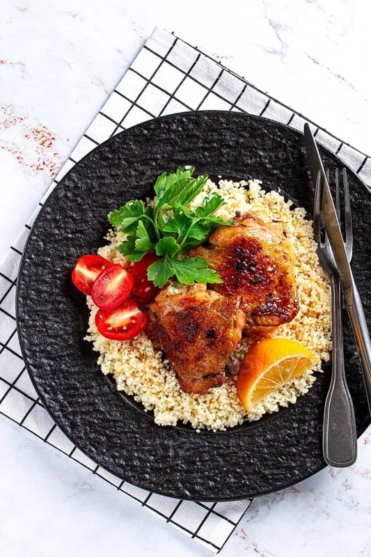 Grilled chicken served with couscous with fresh vegetables and herbs on a black platter, Greek cuisine, homemade