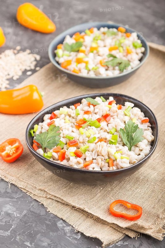 Pearl barley porridge with vegetables in blue ceramic bowls on a black concrete background and linen textile. Side view, close up, selective focus. Russian traditional cuisine