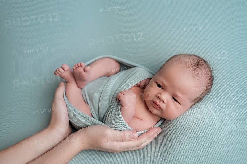 A serene image of a newborn baby gently cradled in an adult's hands. The baby is wrapped in soft, light-colored fabric. The peaceful scene exudes warmth and security