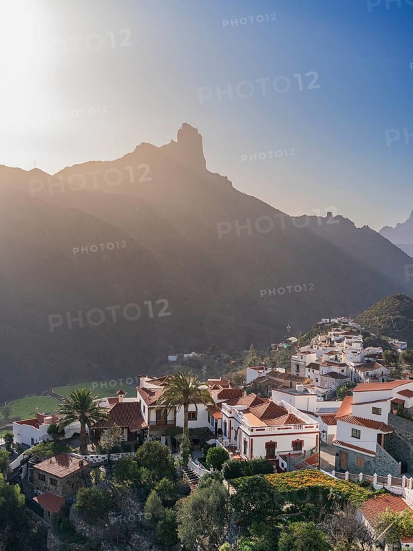 A picturesque scene of Tejeda village in Gran Canaria, capturing the traditional white houses and lush greenery set against the dramatic backdrop of rugged mountains, bathed in the warm glow of a sunset