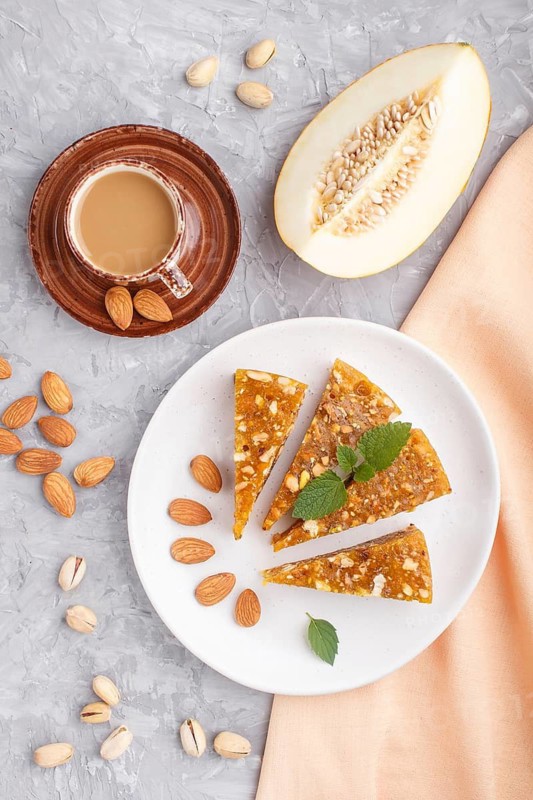 Traditional turkish candy cezerye made from caramelised melon, roasted walnuts, hazelnuts, cashew, pistachios on white ceramic plate and a cup of coffee on a gray concrete background. top view, flat lay, close up