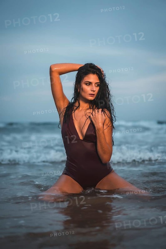 Caucasian brunette in maroon swimsuit, on the beach enjoying the holidays in the sea water on her knees