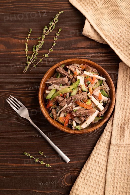 Meat salad with beef and vegetables in wooden bowl on brown wooden background and linen textile. top view, flat lay, close up