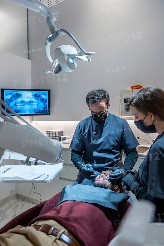 Dentist and assistant wearing masks and gloves performing a dental checkup on a patient in a modern dental clinic