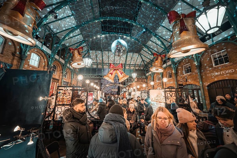 Crowd at a busy Christmas market surrounded by decorative bells and lights, AppleMarket, London, United Kingdom