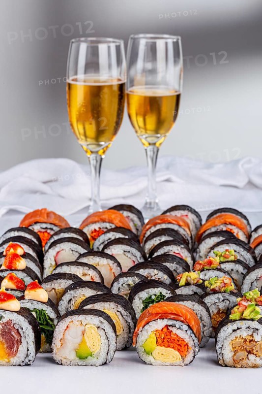 An elegant assortment of sushi rolls with vibrant toppings paired with two glasses of sparkling wine, set on a white background. Perfect for a celebration or gourmet meal