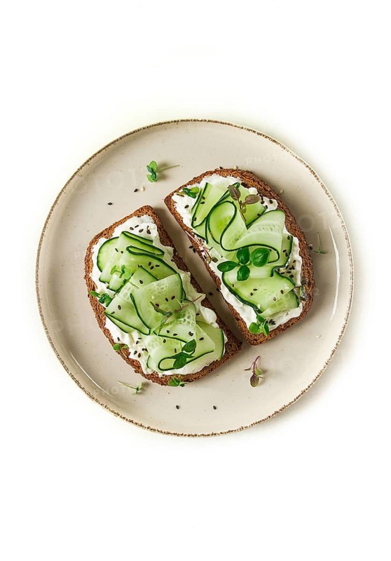 Breakfast, cereal bread sandwiches, cream cheese, sliced cucumber, with micro greenery on a light table, close-up, top view, selective focus, no people