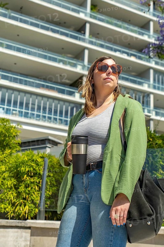 Businesswoman wearing sunglasses holding reusable coffee cup standing near modern building