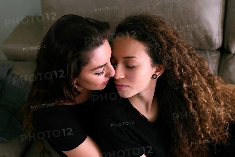 Tender scene of a female gay couple sharing a loving embrace in their cozy living room, one kisses the other's forehead gently