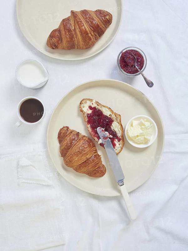 Continental breakfast served on white tablecloth croissants, butter, jam and cup of coffee