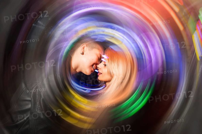 A lesbian couple shares an intimate moment surrounded by a colorful swirl of abstract light. The vibrant hues convey a sense of celebration and joy in their connection