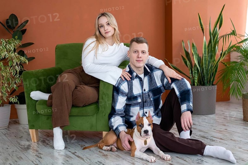 A young man and woman relax at home with their pet dog, sitting on a stylish wooden floor with indoor plants enhancing the background
