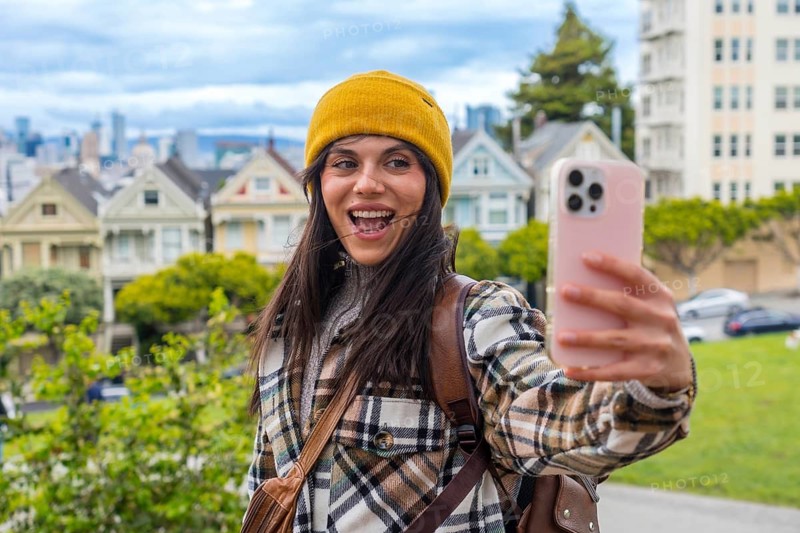 Happy young woman traveling, holding a smartphone and recording a selfie video with the iconic painted ladies houses of san francisco in the background