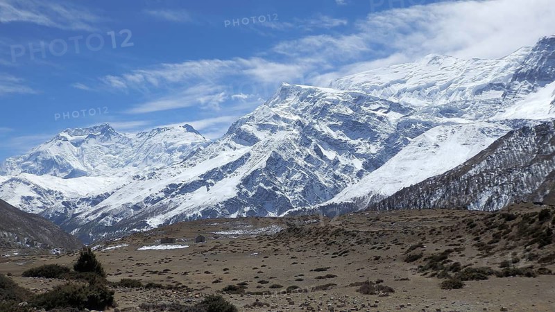 Wide landscape with snow-capped mountains under clear skies, trekking at Annapurna Circuit, Manang, Nepal