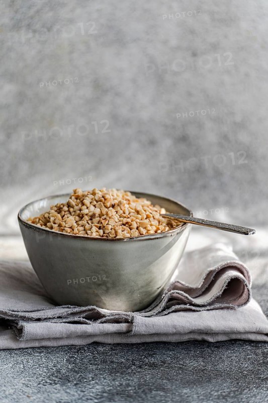 A rustic bowl filled with chopped hazelnuts, resting on a gray textured cloth with a vintage spoon