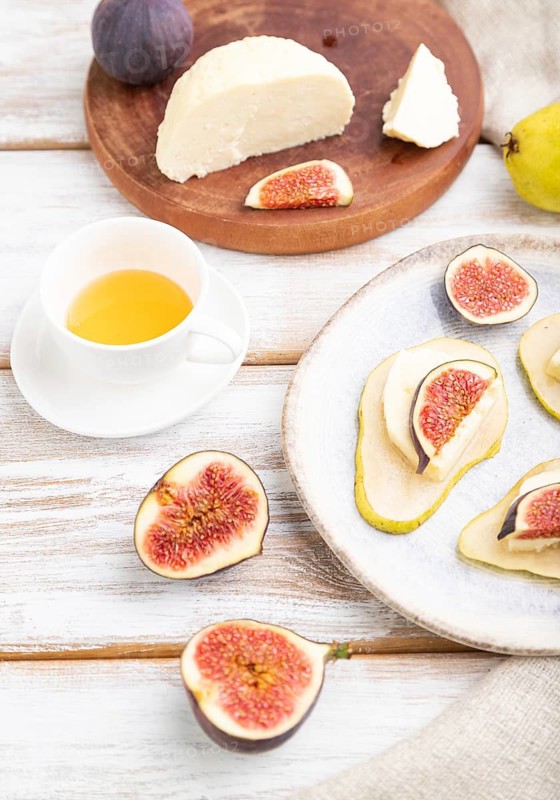 Summer appetizer with pear, cottage cheese, figs and honey on a white wooden background and linen textile. Side view, close up, selective focus