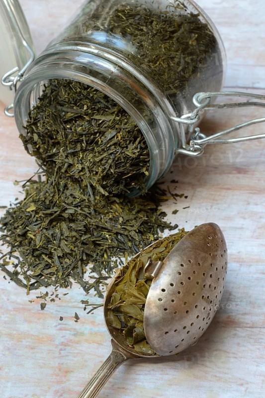 Green tea in storage containers and brewed tea leaves in teaspoons