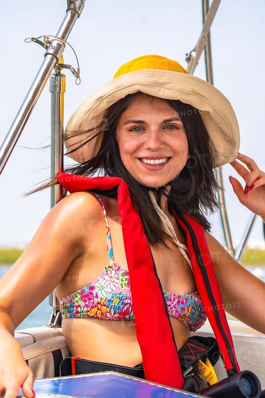 Happy tourist wearing a life jacket, sun hat, and bikini top, enjoying a summer boat trip along the stunning coastline of the algarve region in portugal. Embracing the joy of travel and adventure