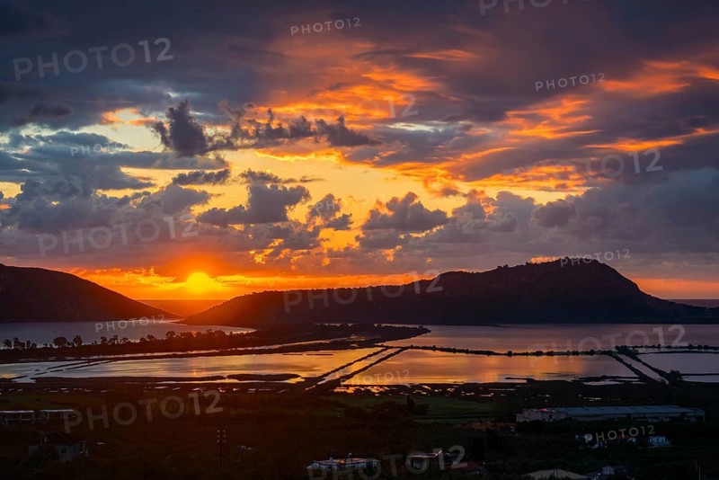 Stunning sunset over Voidokilia Beach and the Divari Lagoon of Pylos, with vivid orange and violet skies reflecting in calm waters, framed by hills and lush coastal landscapes