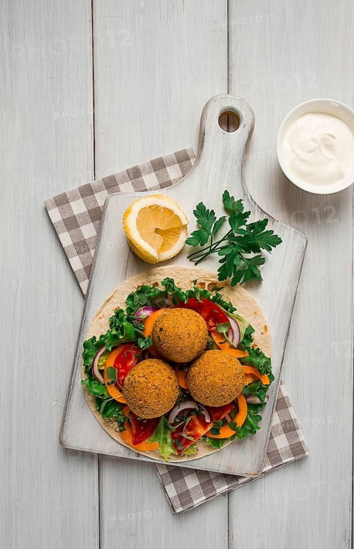 Tortillas, wrapped falafel balls, with fresh vegetables, vegetarian healthy food, on a wooden white background, no people, selective focus