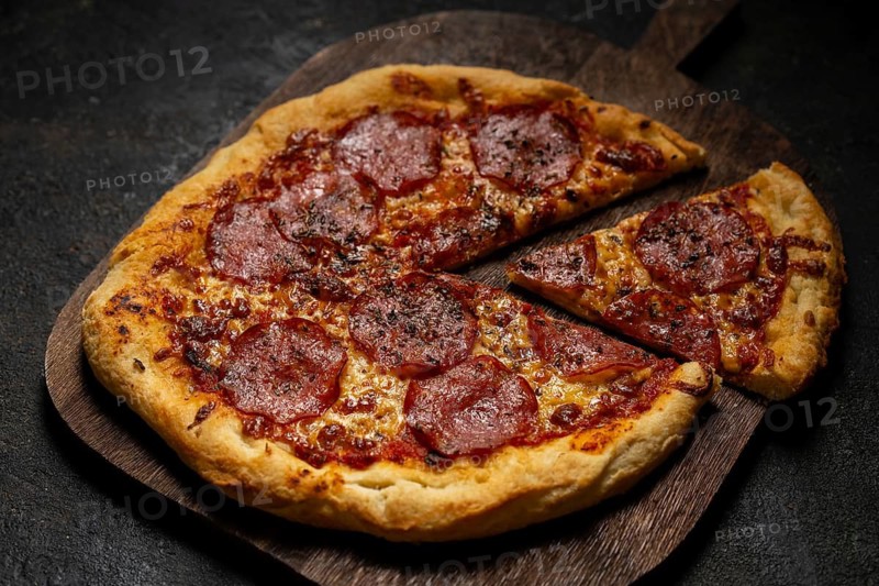 A mouthwatering homemade pepperoni pizza with melted cheese and a crispy crust sits on a wooden board. One slice is cut, showcasing the savory toppings. Perfect for any pizza lover