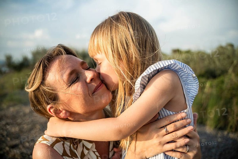 A mother and daughter share a heartfelt embrace on a beautiful summer day in Italy. The little girl kisses her mother's cheek, capturing a moment of love, warmth, and happiness