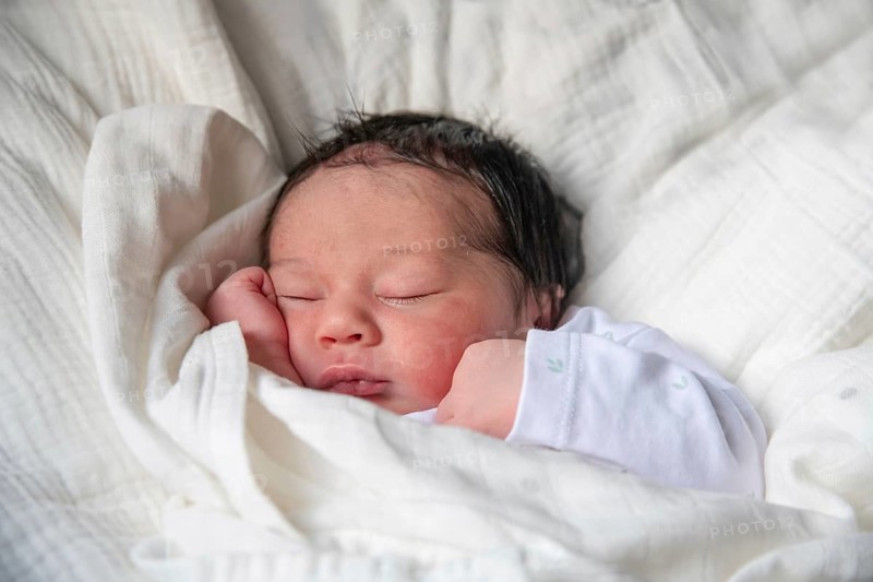 A newborn baby peacefully sleeps wrapped in a soft white blanket, showcasing the tender moments of new life. The close-up image captures warmth, innocence, and tranquility