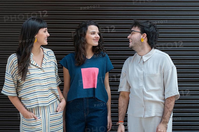 A group of three friends, two women and a man, are enjoying a light-hearted conversation outdoors in front of a textured wall, displaying diversity and friendship